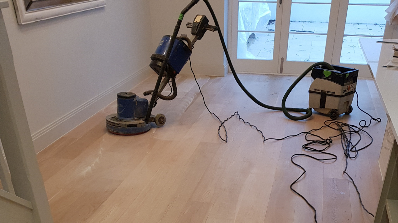 Commercial Floor Sanding in Upminster: dust-free sanding of pale solid oak hardwood plank flooring with a buffer and HEPA vacuum near French doors.