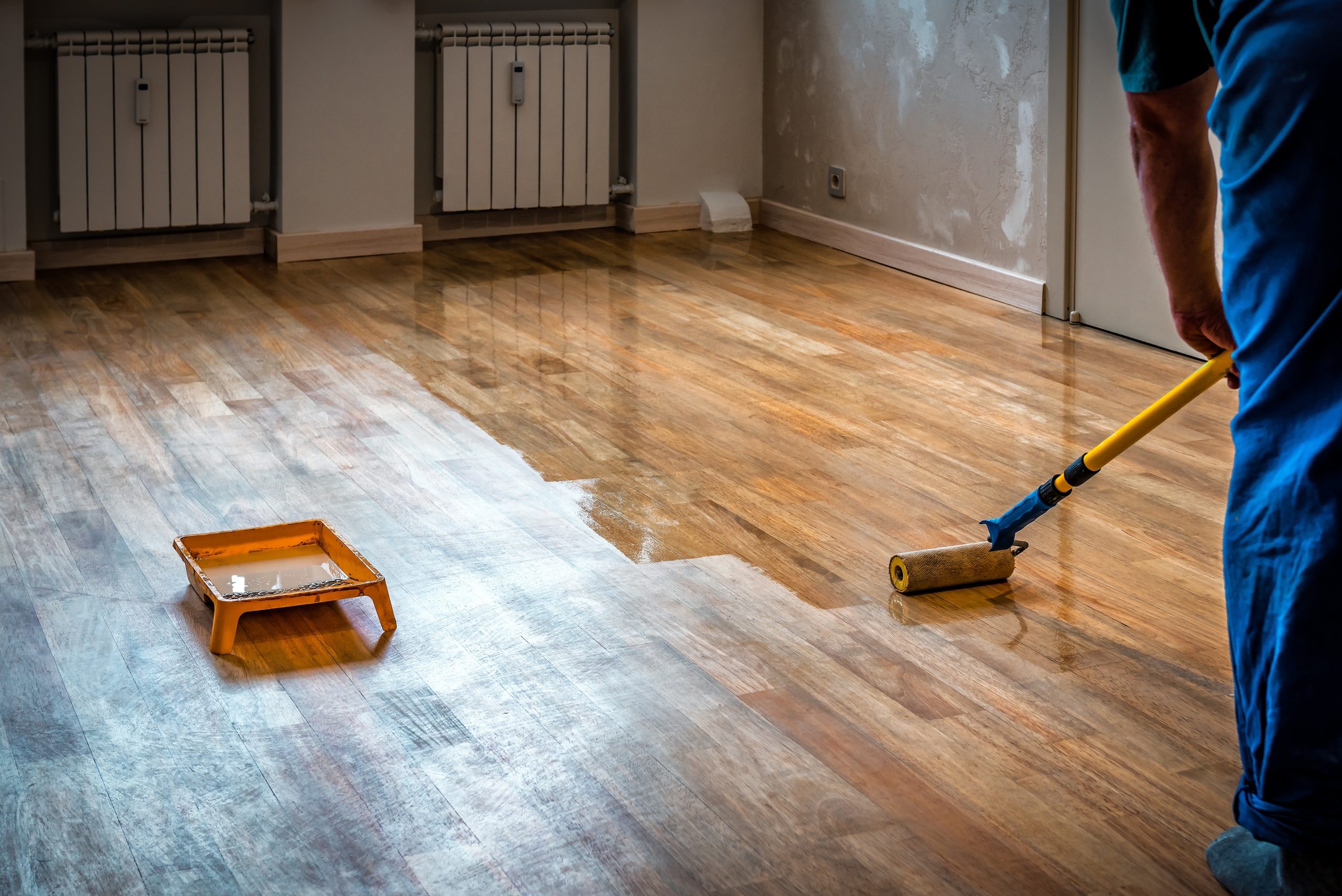 Commercial Floor Sanding in Upminster: technician rolling clear lacquer onto freshly sanded oak hardwood plank flooring, keeping a wet edge for an even finish.